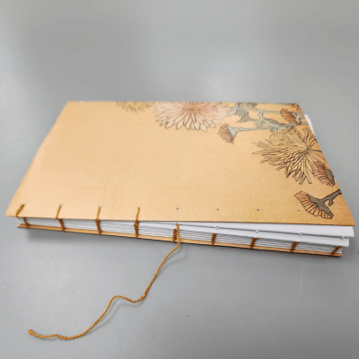 A handmade book with a light brown cover featuring flowers, partially bound.